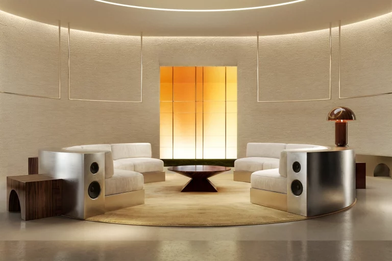 NOVU circular listening salon by NOCOD Studio — full view. Two facing curved sofas, round silk carpet, dark wood coffee table, amber LED wall, copper mushroom lamp. Immersive retail concept.